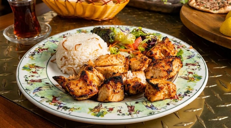Grilled chicken shish tawook with rice, salad, and a glass of tea on a decorative plate.