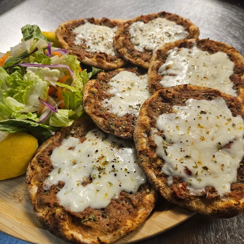 A wooden board with several mini pizzas topped with cheese and herbs, served with a side salad and lemon.