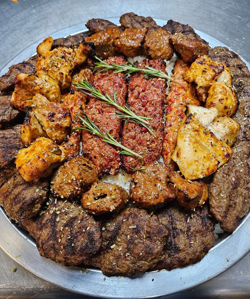 A large platter of various grilled meats, including kebabs, chicken, and ground meat patties, garnished with rosemary.